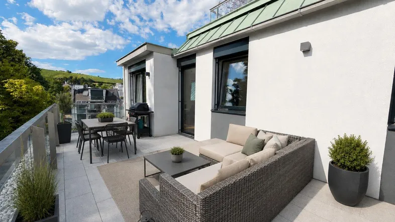 Große Dachterrasse mit modernen Gartenmöbeln und weitem Blick auf die grüne Umgebung unter blauem Himmel.