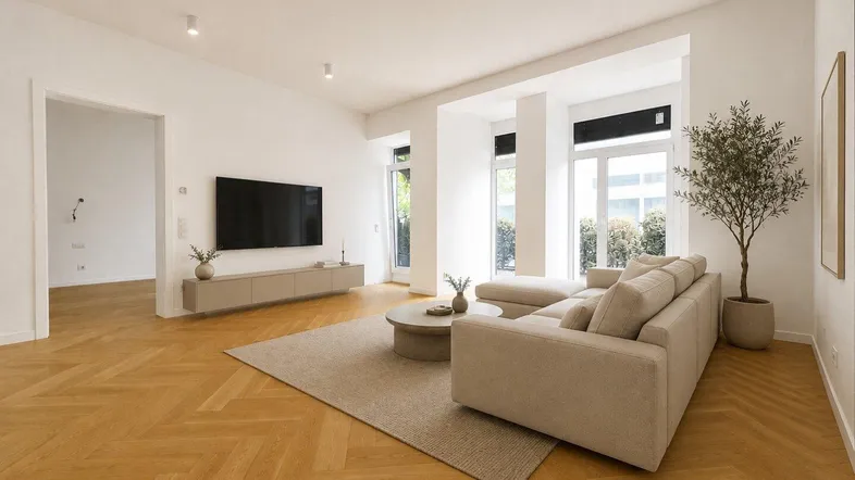 Helles, modern inszeniertes Wohnzimmer mit Fischgrätparkett, großen Fenstern und Zugang zum Außenbereich.