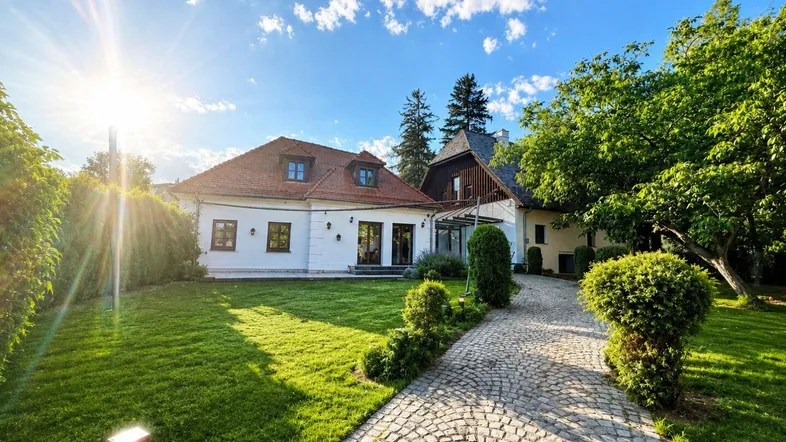 Großzügiges Anwesen mit gepflegtem Garten, Kopfsteinpflasterweg und sonnigem Himmel.