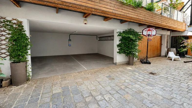 Offene Garage mit gepflastertem Vorplatz, Basketballkorb und begrüntem Dachbereich.