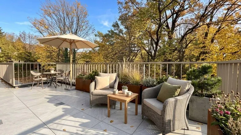 Geräumige Dachterrasse mit bequemen Loungemöbeln und Sonnenschirm, umgeben von herbstlicher Natur.