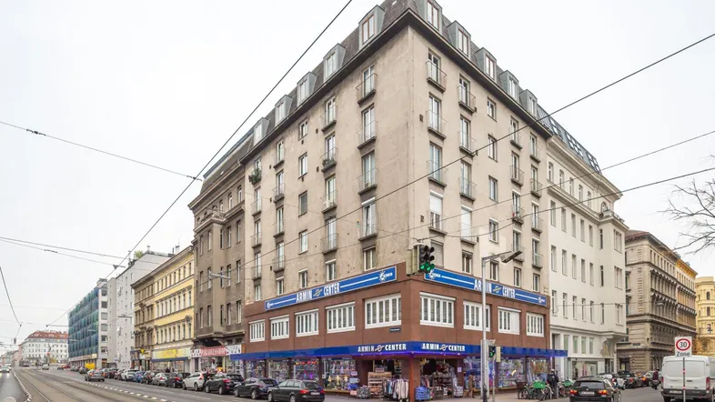 Großes Eckgebäude mit mehreren Stockwerken und einem Geschäft im Erdgeschoss an einer belebten Straße.