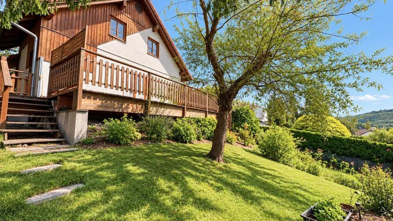 Charmantes Haus mit Holzfassade und großem Gartenbereich, umgeben von grüner Natur und Bäumen.