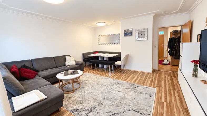 Gemütlicher Wohn- und Essbereich mit dunklem Sofa, hellem Teppich und integrierter Essecke.