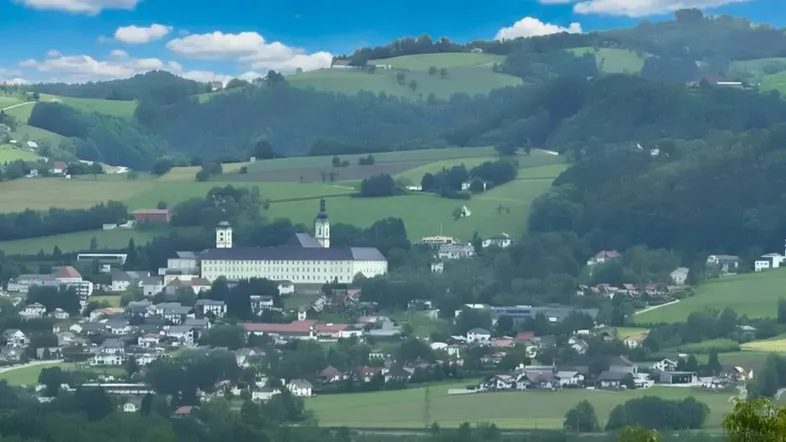 Panoramablick auf eine malerische Stadt mit einem historischen Gebäude inmitten grüner Hügel.