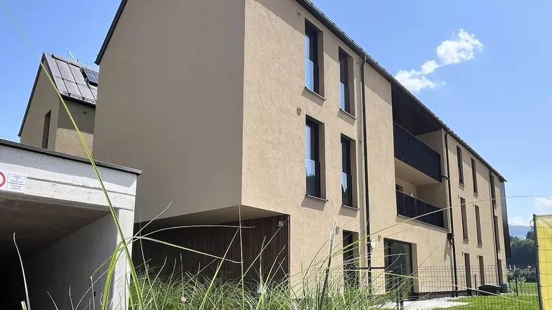 Modernes Mehrfamilienhaus mit beiger Fassade, Balkonen und Tiefgaragenzufahrt unter blauem Himmel.