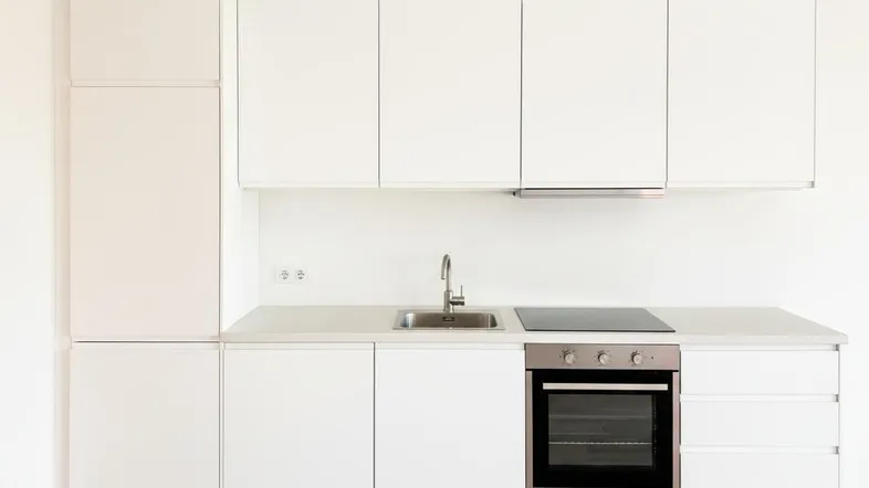 Moderne, kompakte weiße Küchenzeile mit integriertem Backofen und Induktionskochfeld auf Holzdielenboden.