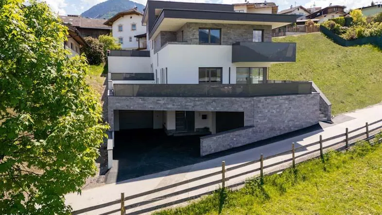 Modernes Wohnhaus mit mehreren Etagen, Balkonen und integrierter Garage in Hanglage.