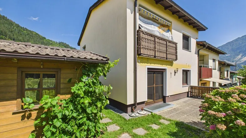 Außenansicht eines Hauses mit Balkon, kleiner Terrasse und einem charmanten Holzschuppen im Grünen.
