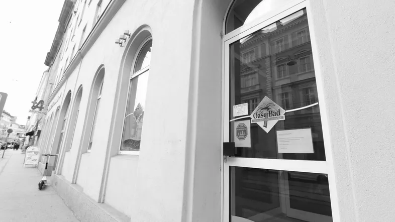 Schwarz-Weiß-Aufnahme der Gebäudefassade mit gewölbten Fenstern und einem Glaseingang an einer Straße.