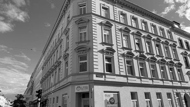 Schwarz-Weiß-Aufnahme eines historischen Eckgebäudes mit vielen Fenstern und Geschäften im Erdgeschoss.