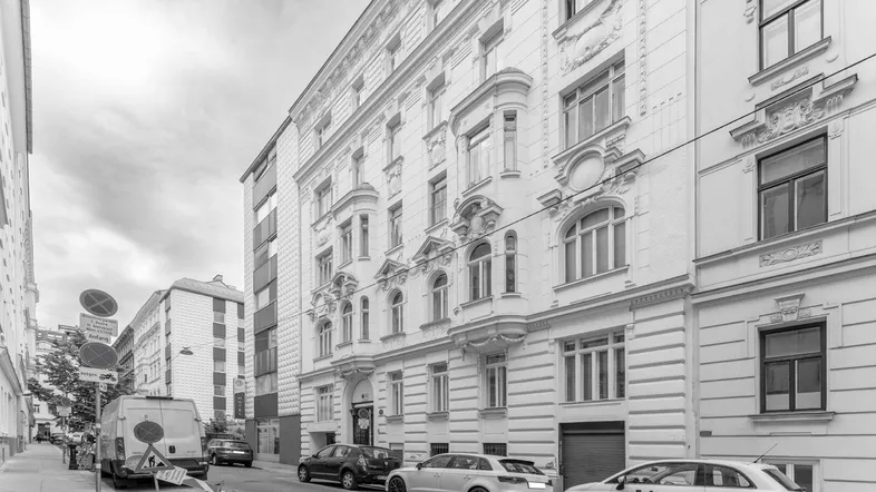 Historisches Gebäude mit reich verzierter Fassade und parkenden Autos auf der Straße.