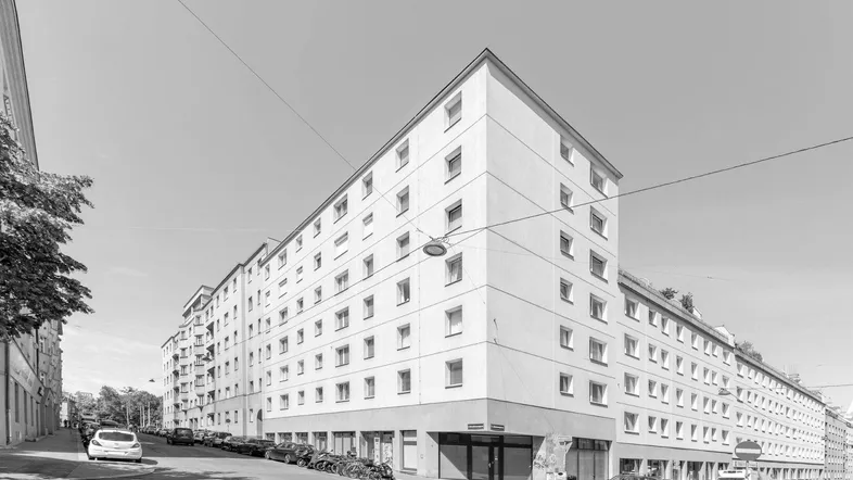 Schwarz-Weiß-Aufnahme eines Mehrfamilienhauses mit vielen Fenstern und Geschäften im Erdgeschoss.