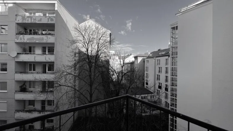 Blick vom Balkon auf umliegende Wohngebäude und Bäume in Schwarz-Weiß.