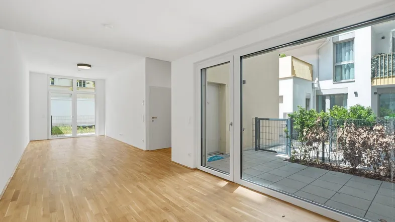 Geräumiger, leerer Wohn-Essbereich mit großen Fenstern und Zugang zu einer Terrasse.