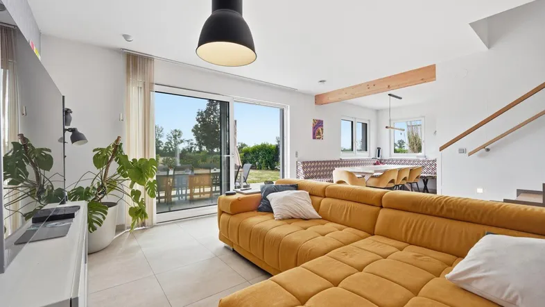 Helles Wohnzimmer mit gelbem Sofa, Fliesenboden und Zugang zur Terrasse mit Gartenblick.