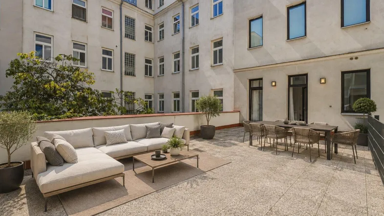 Große, möblierte Terrasse mit bequemer Sitzecke und Esstisch, umgeben von der Gebäudefassade.