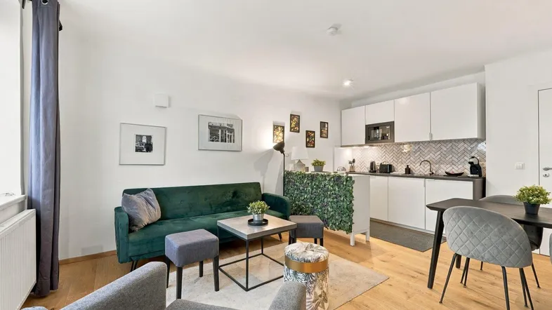 Moderne offene Wohnküche mit grüner Couch, Holzboden und integrierter Küchenzeile.