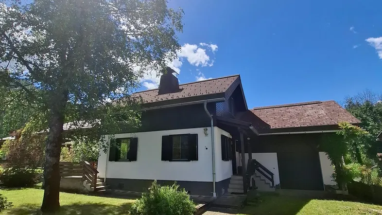 Vorderansicht eines Hauses mit gepflegtem Rasen, Bäumen und einem gepflasterten Weg unter blauem Himmel.