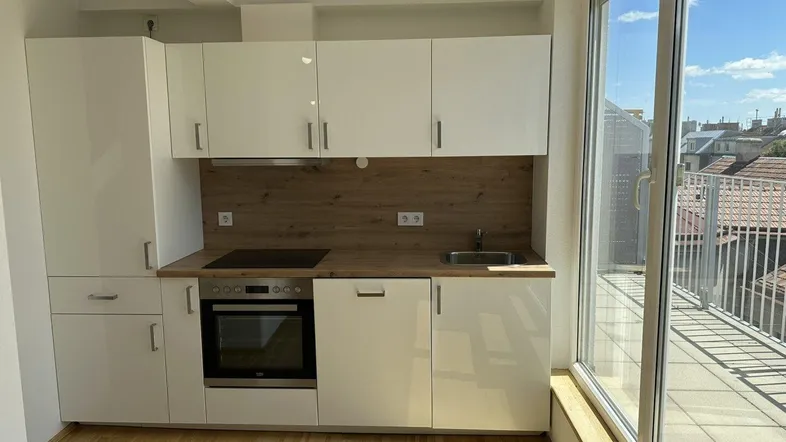 Moderne Einbauküche mit weißen Hochglanzfronten, Holzarbeitsplatte und Zugang zum Balkon.