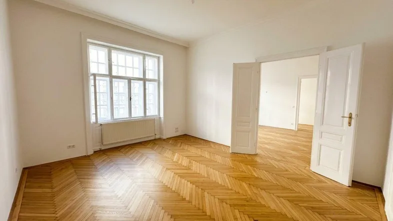 Heller, geräumiger Raum mit klassischem Fischgrätparkett, hohen Decken und großen Fenstern.