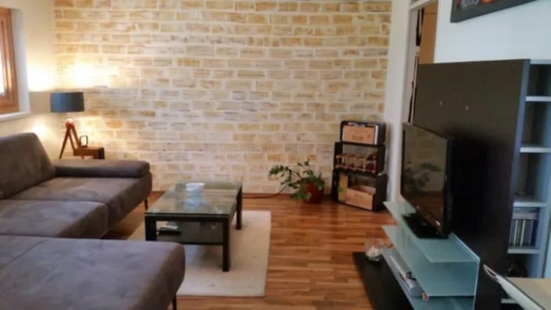 Gemütliches Wohnzimmer mit beiger Ziegelwand, Holzboden und modernem Sofa.