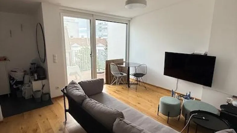 Wohnzimmer mit Sofa, Essbereich und Zugang zu einem Balkon durch eine große Glastür.