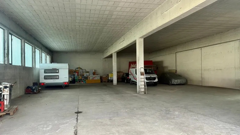 Geräumige Lagerhalle mit Betonboden, hohen Decken und großen Fenstern, ideal für Fahrzeuge und Lagerung.