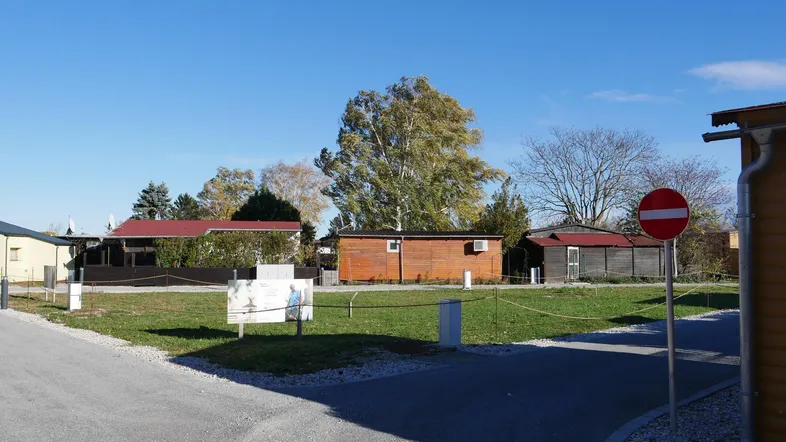 Blick auf kleine Holzhäuser und grüne Rasenflächen unter blauem Himmel in einer Ferienanlage.
