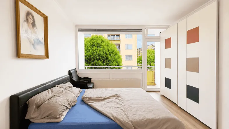 Schlafzimmer mit Doppelbett, Einbauschränken und Balkonzugang mit Blick ins Grüne.