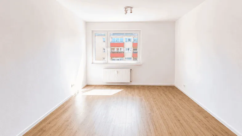 Helles Zimmer mit Laminatboden, weißen Wänden und Blick auf umliegende Gebäude.