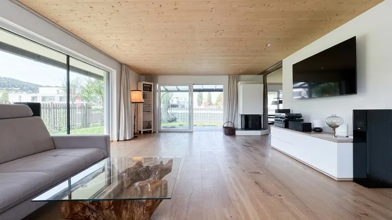 Helles Wohnzimmer mit Holzboden, Kamin und großen Fenstern mit Blick ins Grüne.