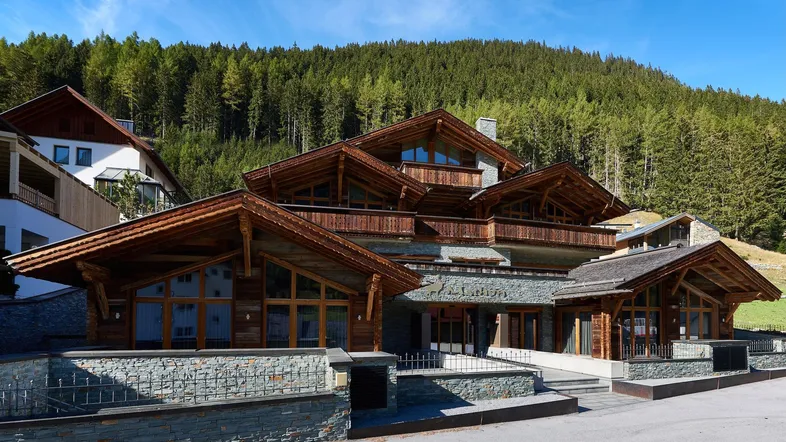 Luxuriöses Chalet mit traditioneller Holzfassade und Steinelementen vor bewaldeter Bergkulisse.