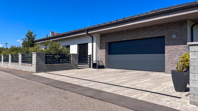 Moderne Hausfassade mit Doppelgarage und gepflasterter Einfahrt unter blauem Himmel.
