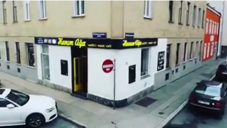 Außenansicht eines Eckgebäudes mit einem Geschäft im Erdgeschoss und parkenden Autos auf der Straße.