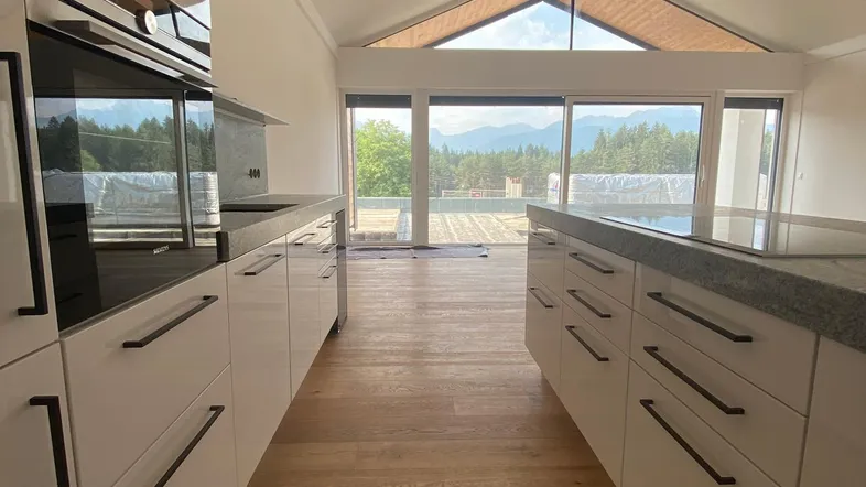 Moderne Küche mit weißen Schränken, Granitarbeitsplatten und Holzboden, mit Blick auf die Berge.