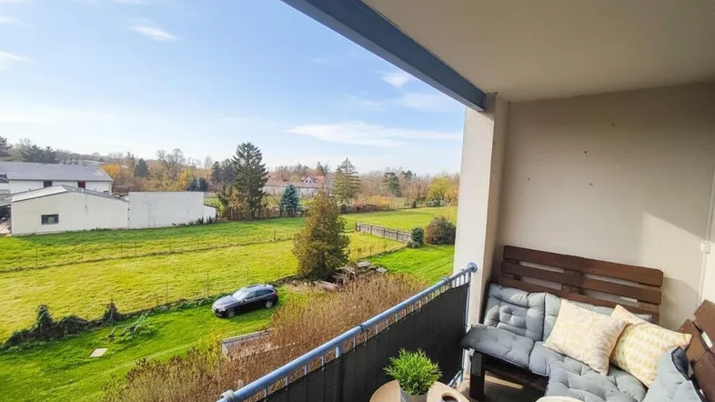 Gemütlicher Balkon mit Sitzgelegenheiten und weitem Blick ins Grüne unter blauem Himmel.