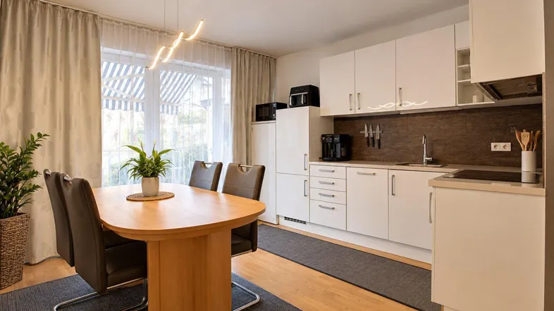 Moderne Küche mit weißen Schränken, Essbereich und Zugang zum Balkon.