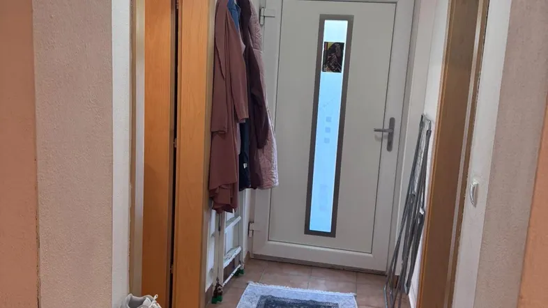 Heller Eingangsbereich mit Fliesenboden, Garderobe und Schuhregal, der zu weiteren Räumen führt.