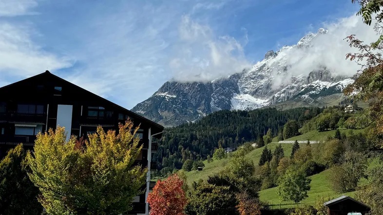 Gebäude mit alpiner Architektur und schneebedeckten Bergen im Hintergrund unter blauem Himmel.