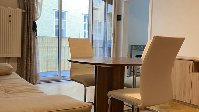 Heller Wohn- und Essbereich mit Parkettboden, Sofa und Zugang zum Balkon.