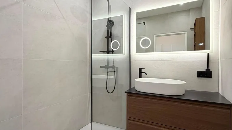 Modernes Badezimmer mit ebenerdiger Dusche, beleuchtetem Spiegel und elegantem Waschtischunterschrank.