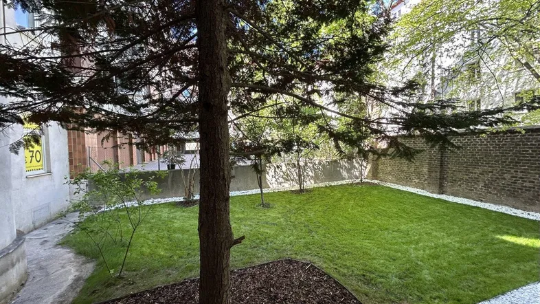 Gepflegter Gartenbereich mit Rasenfläche, Bäumen und einer Backsteinmauer im Innenhof.