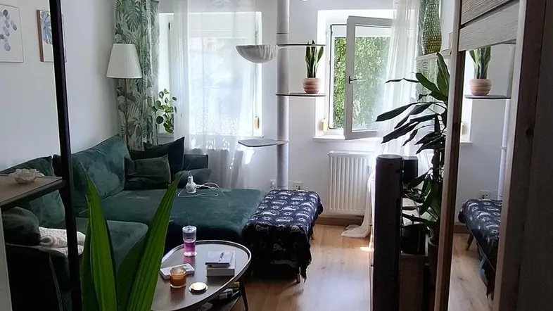 Helles Wohnzimmer mit gemütlichem Sofa, Holzboden und Blick auf den Garten durch das Fenster.