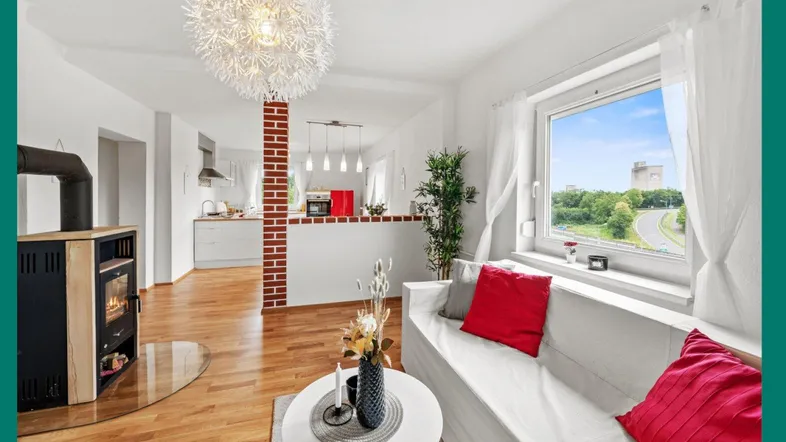 Helles Wohnzimmer mit Holzboden, Kaminofen und offenem Übergang zur modernen Küche.