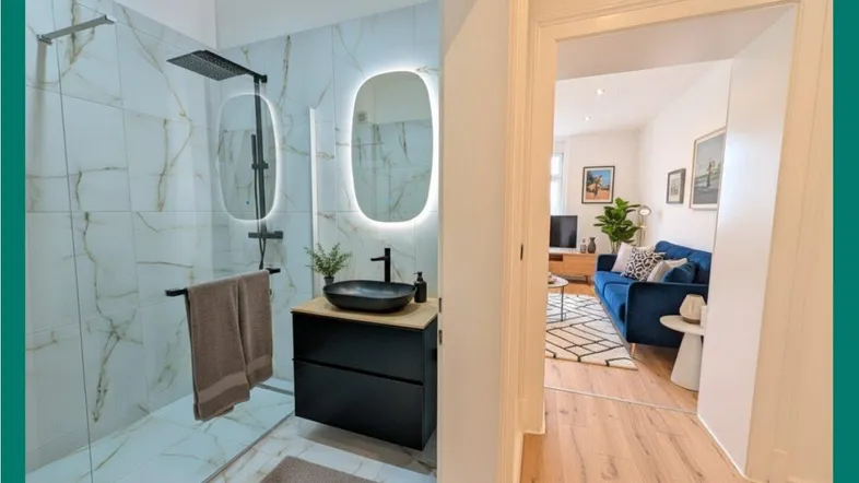 Modernes Badezimmer mit begehbarer Dusche, beleuchtetem Spiegel und Blick in den Wohnbereich.