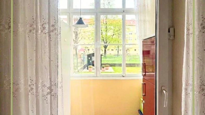 Blick aus einem Innenraum auf einen verglasten Balkon mit Fensterfront und Tageslicht.