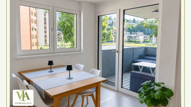 Heller Essbereich mit Holztisch, weißen Stühlen und Zugang zu einem möblierten Balkon.