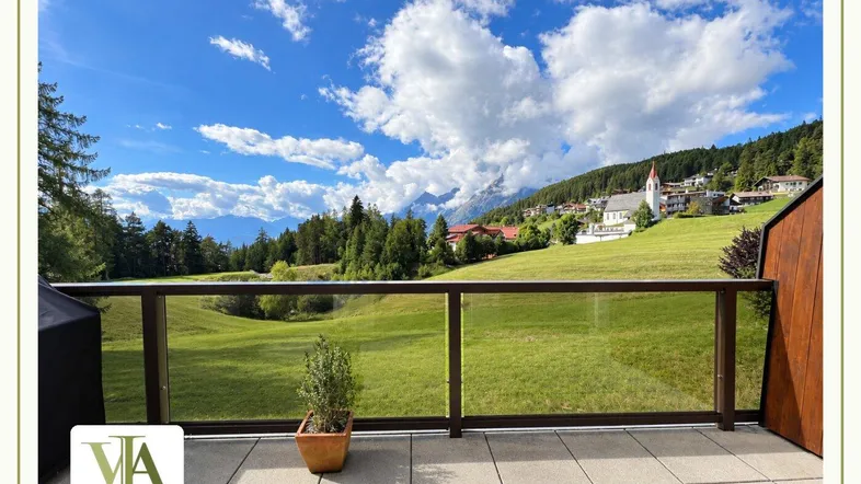 Geräumige Terrasse mit Glasgeländer bietet einen weiten Blick auf die umliegende Berglandschaft und ein Dorf.