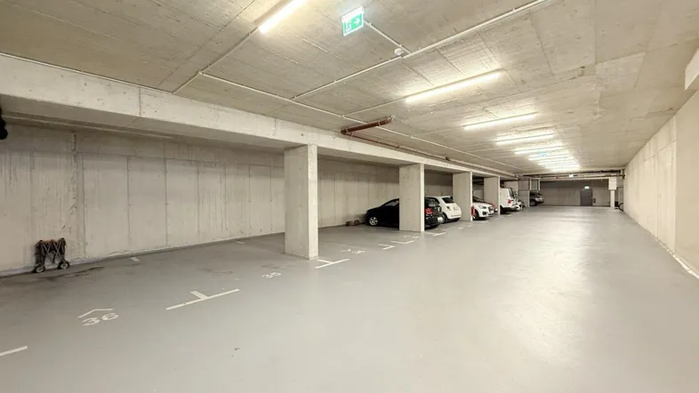 Tiefgarage mit mehreren Stellplätzen, Betonwänden und Decken sowie heller Beleuchtung.